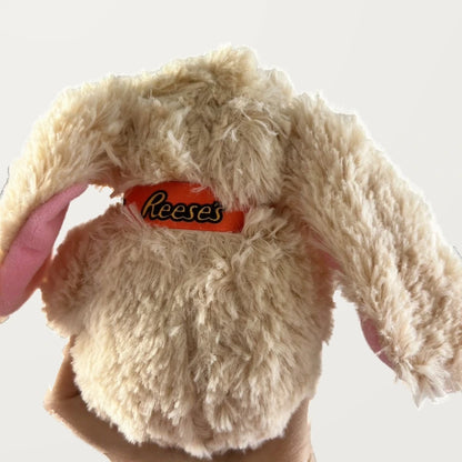 Back view of a beige floppy-ear bunny plush showing its textured fur, pink ear lining, and orange neck ribbon.