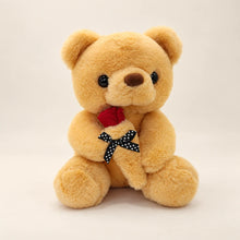 Angled front view of a seated golden teddy bear holding a red fabric rose.