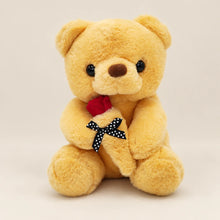 Front view of a golden teddy bear holding a red fabric rose with a black and white polka dot bow.