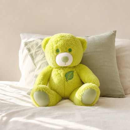 Lime green leaf teddy bear plush sitting on a bright cream bed