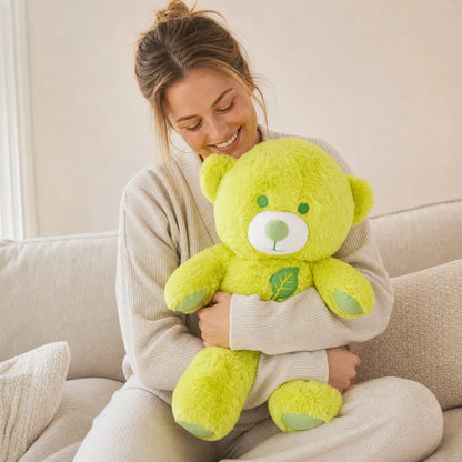 Woman hugging a large lime green leaf teddy bear plush on a cream sofa
