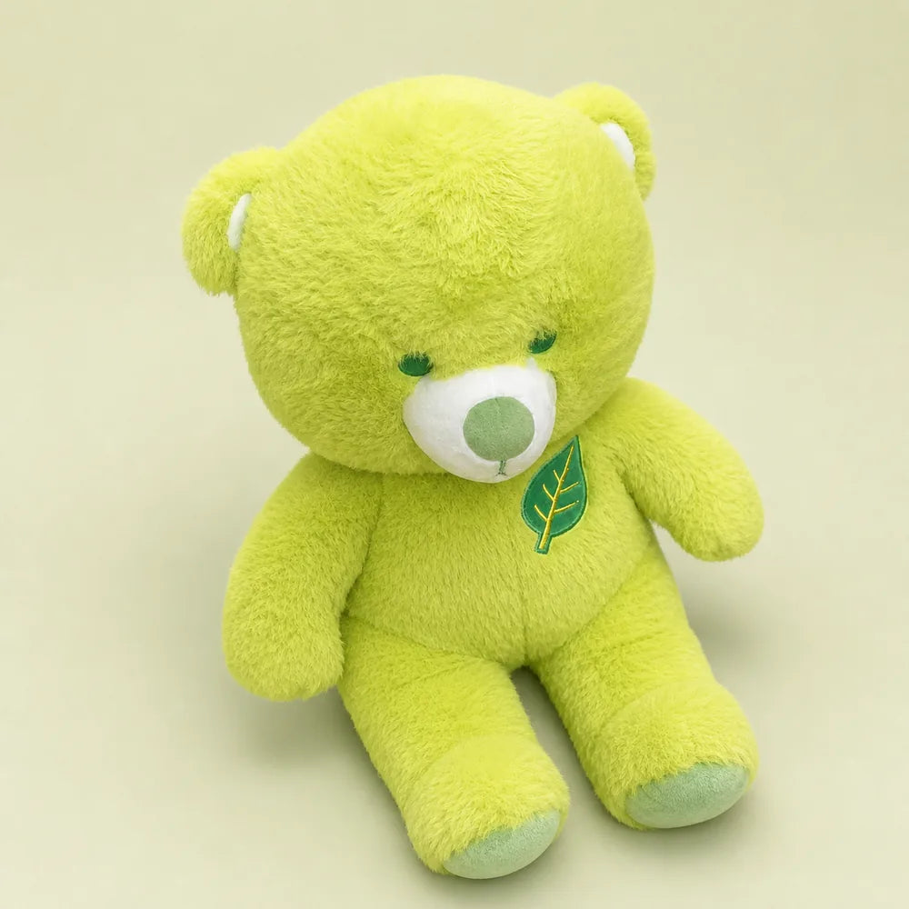 Lime green leaf teddy bear plush in an angled seated view on a soft sage studio backdrop