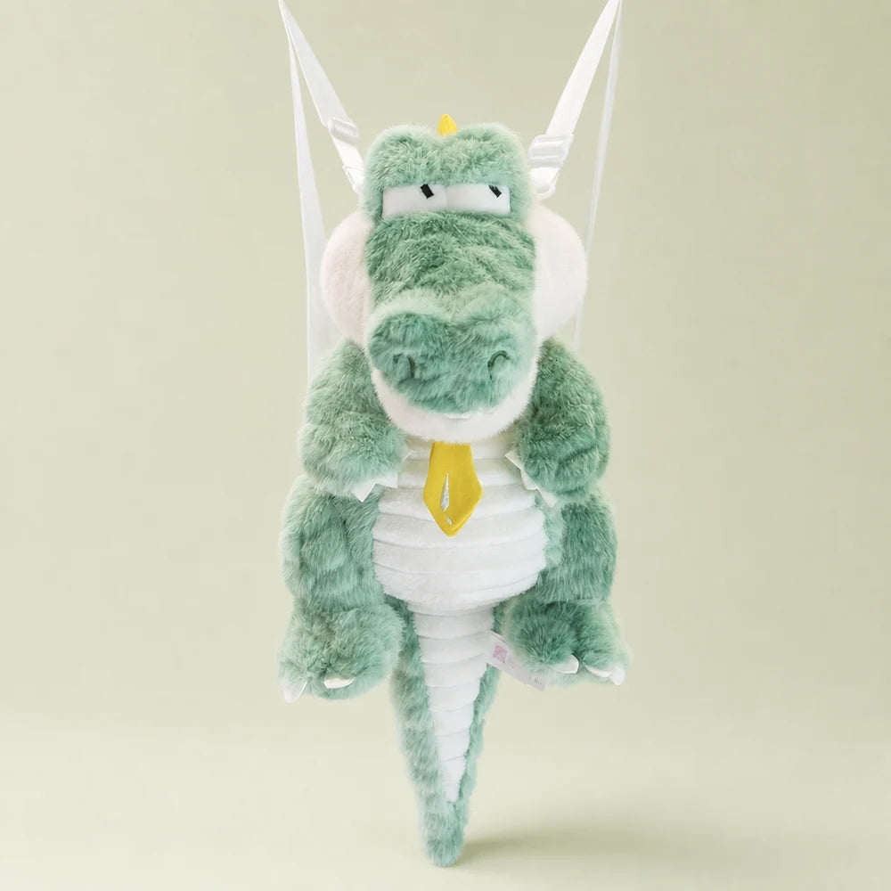 Mint green crocodile plush backpack with visible white shoulder straps on a sage studio backdrop