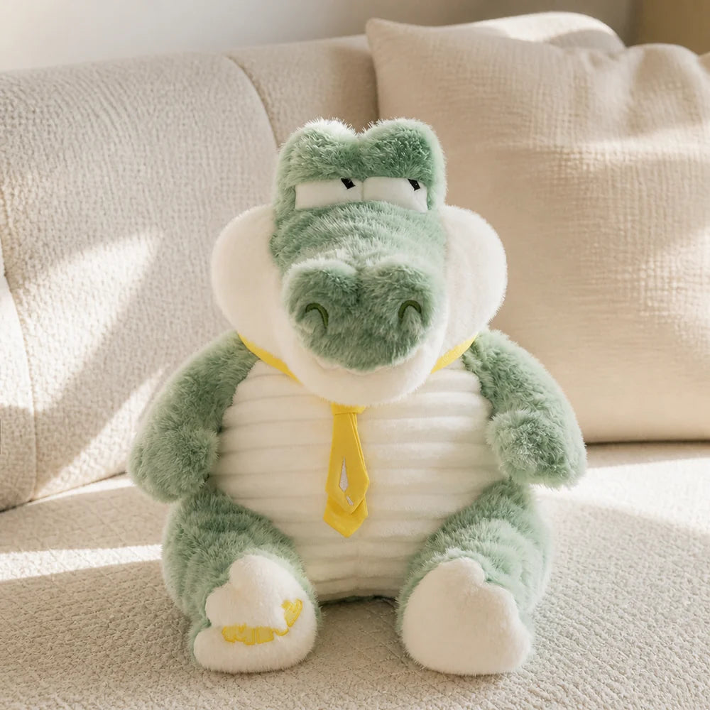 Mint green crocodile sitting plush with yellow tie on a cream sofa
