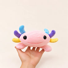 Front view of the Pastel Gills pink axolotl plush held in one hand, with glossy black eyes and blue, purple, and yellow gills.
