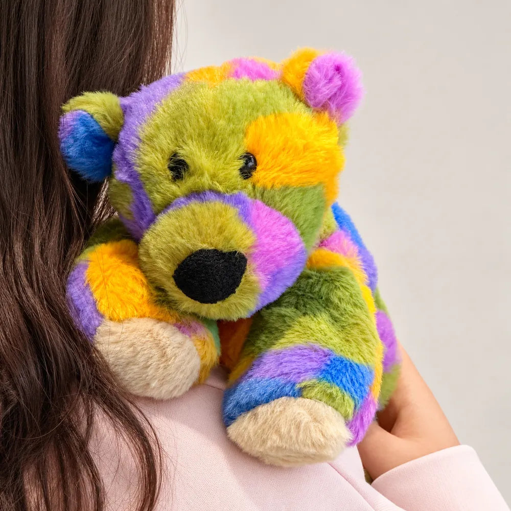 Close-up of a rainbow bear plush being hugged, showing its black nose and soft faux fur.
