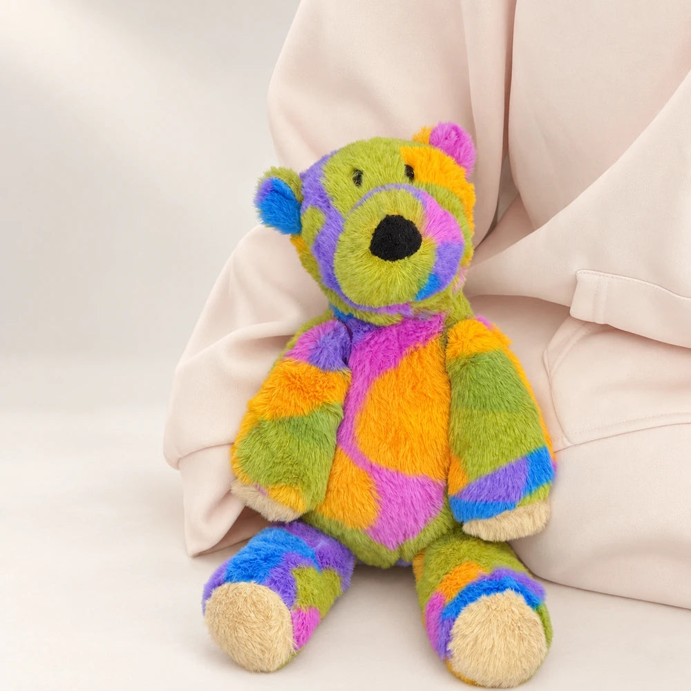 Rainbow bear plush sitting with its cream-colored foot pads facing forward.