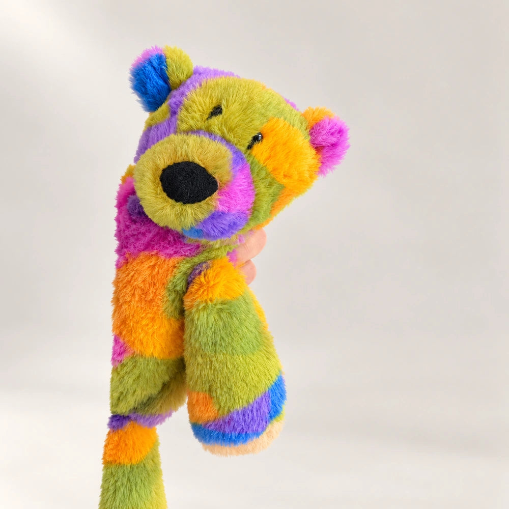 Rainbow bear plush with its head tilted, showing its round ears, black nose, and multicolored fur.